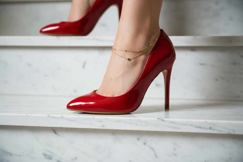 Ein Frauen Fuß trägt eine fußkette mit einem herzanhänger und kleinen kugeldetails