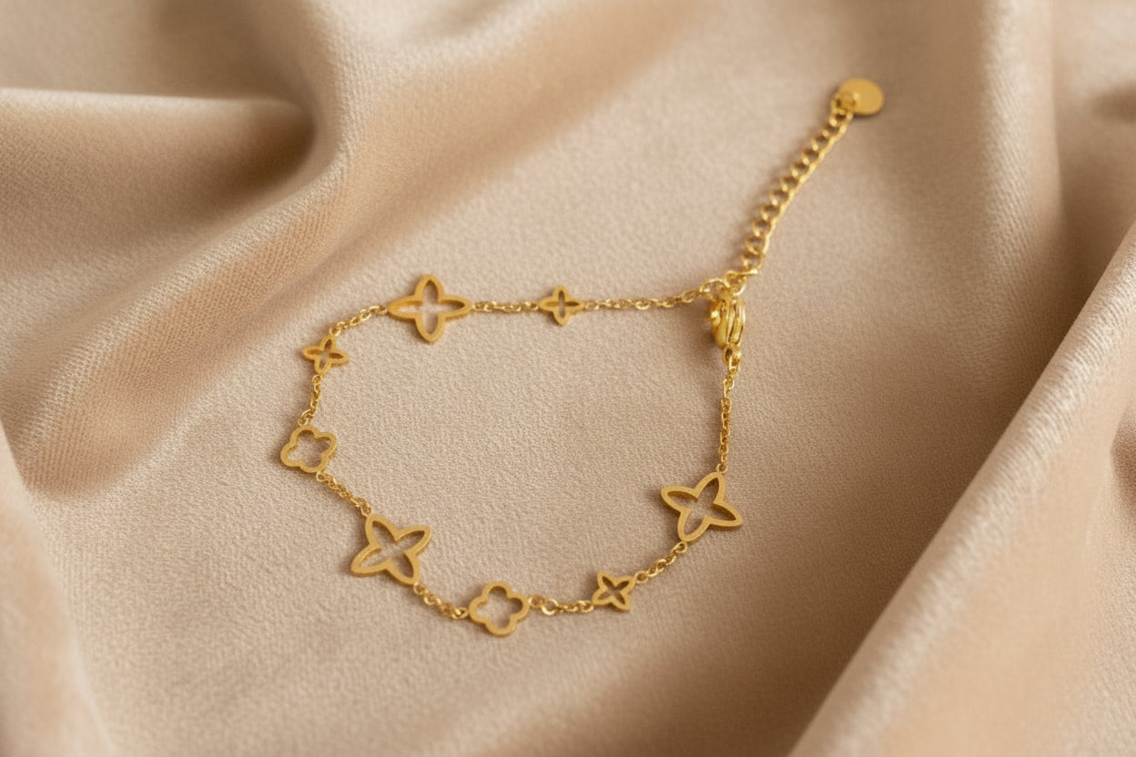 Ein Armband Gold mit verschiedenen Sternen liegt auf ein beigefarbenes samt tuch