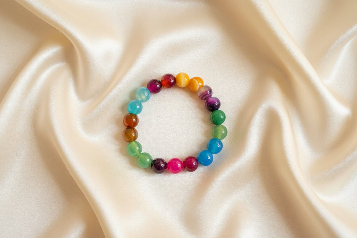 Ein buntes Acat Perlenarmband liegt auf ein beige seidenes Tuch